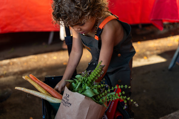 Child carrying a paper bag of fresh basil and vegetables